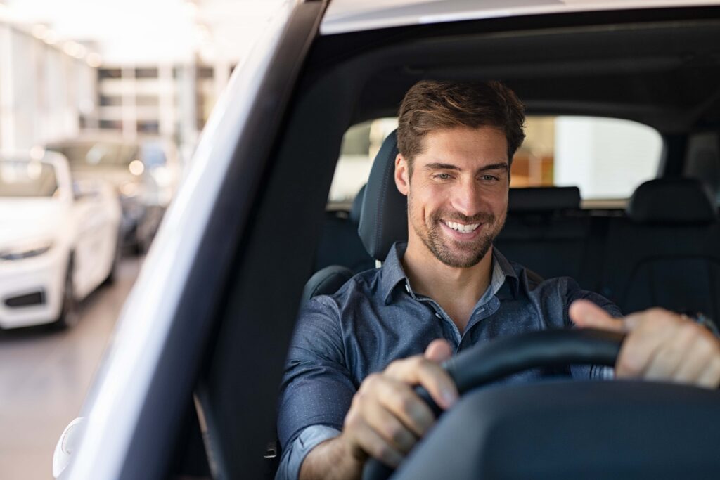 person smiling whilst test driving a new car next to a car dealership