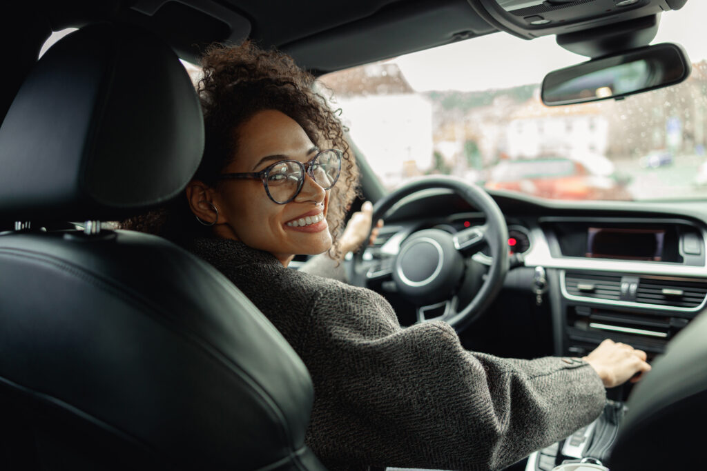 Woman driving car with one hand on steering wheel and another on gear lever and