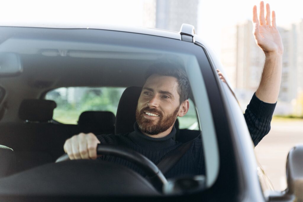 man waving after getting in his car with a smile on his face